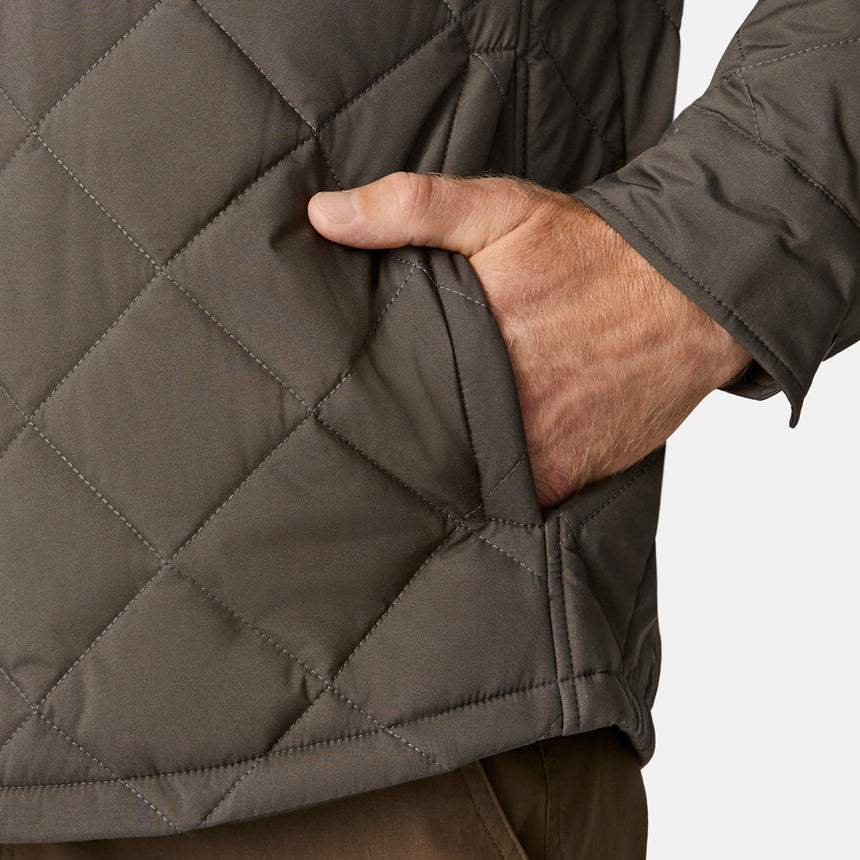 [Kolby is 6'2" wearing size M.] Men’s Free Country quilted jacket in brown with diamond pattern stitching—features a zippered left chest pocket, button front closure, and side hand pockets. Styled over a light gray shirt and paired with brown pants for a rugged, polished outdoor look.