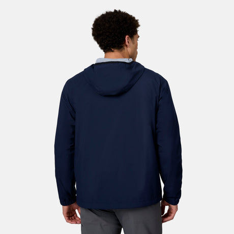 A man with short curly hair is seen from behind, wearing the Free Country Men's Agile II Windshear Jacket in navy blue and gray pants, standing against a plain light background.