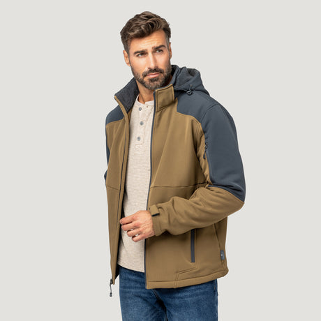 A man with brown hair and a beard wears the Men's Flat Lands Hurricane Softshell® Jacket by Clearance in tan and gray over a light beige henley and blue jeans, standing against a plain light gray background.
