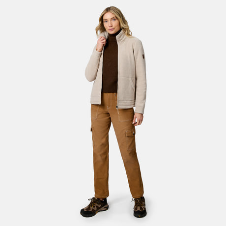 A woman modeling a light beige fleece jacket over a dark brown turtleneck, paired with brown cargo pants and brown hiking boots, against a plain light gray studio background.