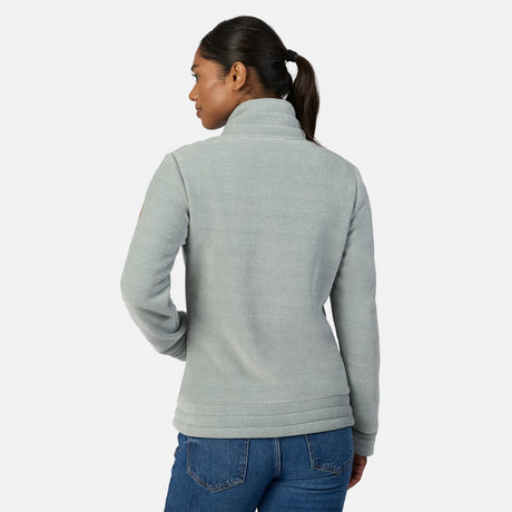[Model is wearing size S.] A woman modeling the back of a light green heather zip-up fleece jacket with a mock neck collar, paired with blue jeans, against a plain light gray studio background.