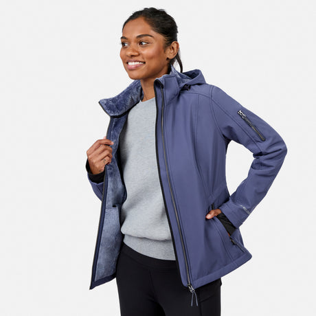 [Model is wearing size S.] A woman wearing a slate blue hooded jacket with a plush lining, layered over a gray sweater and black pants, photographed against a light gray studio background.