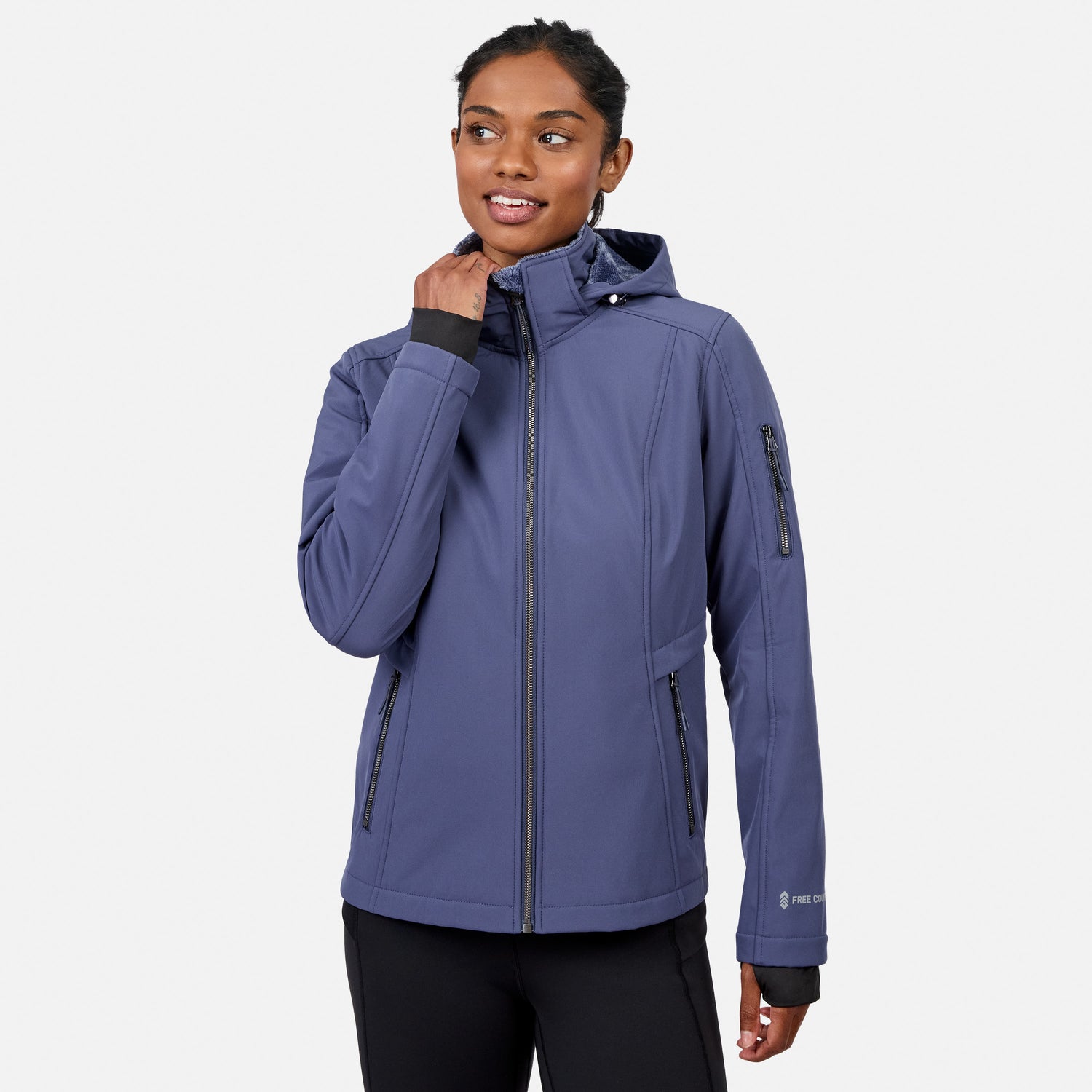 [Model is wearing size S.] A woman wearing a slate blue hooded softshell jacket with black zipper details and black pants, standing against a light gray studio background.