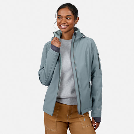 [Model is wearing size S.] A woman wearing a sage green hooded softshell jacket over a gray sweater and brown pants, standing against a light gray studio background.