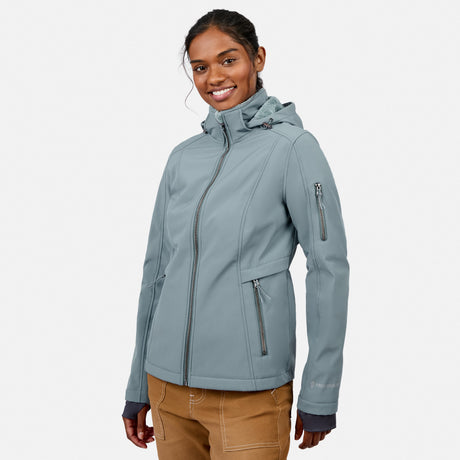 [Model is wearing size S.] A woman wearing a light blue-gray hooded softshell jacket with multiple zippered pockets, paired with tan pants, photographed against a clean light gray studio background.