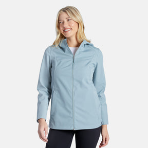 A smiling woman with long blonde hair wears the Clearance Women's Anorak Softshell Jacket in light blue over a white shirt and black pants, standing against a plain white background.
