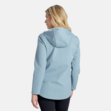 A blonde woman stands with her back to the camera against a plain background, wearing the Clearance Women's Anorak Softshell Jacket in light blue and black pants.