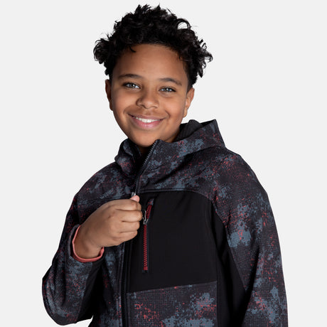 [Model is wearing size M.] Model wearing a red, black, and gray digital camo Free Country jacket featuring contrast side panels, zippered chest pocket, and full front zip; styled with denim for a bold, performance-ready outdoor look.