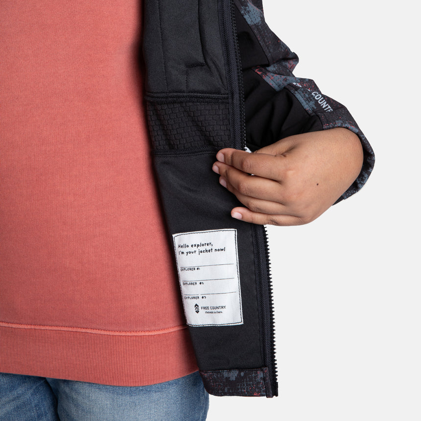 [Model is wearing size M.] Model wearing a red, black, and gray digital camo Free Country jacket featuring contrast side panels, zippered chest pocket, and full front zip; styled with denim for a bold, performance-ready outdoor look.