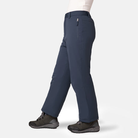 A person models the Free Country Kids' Padded Ski Pant in dark blue with black hiking boots and a white top, standing against a plain light background. The view is from mid-torso down, with their left leg slightly forward.