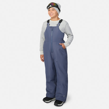 Smiling child wearing blue Kids' Half Pike Ski Bib Pant with black straps, gray knit hat and ski goggles