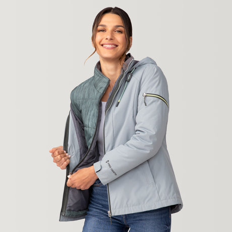 [Olga is 5’9” wearing a size Small.] Woman wearing Free Country Women's Back of Bell 3-in-1 Systems Jacket in light blue with a full front zipper opening, soft lining, attached hood with adjustable drawcords, and water resistant and wind resistant stretch performance fabric, inner puffer jacket, outer shell for weather, light grey background. Perfect women’s  jacket for fall weather.