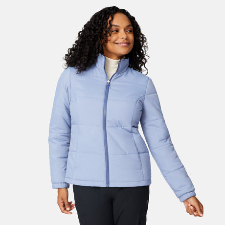 A woman with curly hair, smiling against a plain white background, wears the Free Country Women's Back of Bell 3-in-1 Systems Jacket in light blue and black pants.