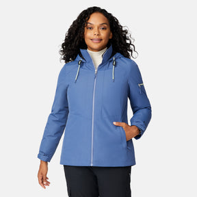 A woman wearing the Free Country Women's Back of Bell 3-in-1 Systems Jacket in light blue, featuring a front zipper and zippered sleeve pocket, stands smiling with one hand in her pocket against a plain white background.