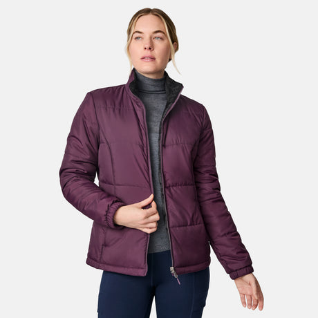 A woman models the Free Country Women's Back of Bell 3-in-1 Systems Jacket in purple over a gray turtleneck, standing against a white background and looking to the side while holding the jacket’s zipper.