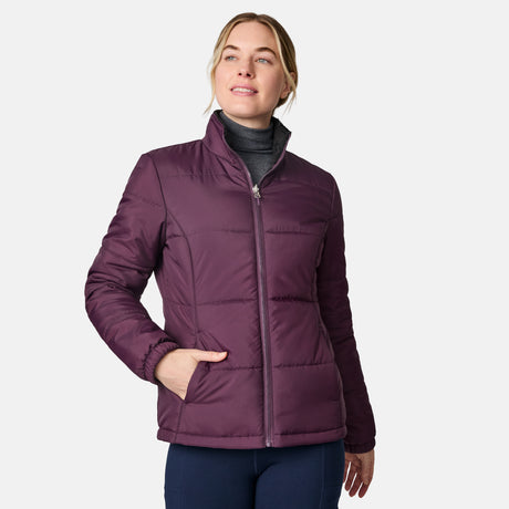 A woman wears the Free Country Women's Back of Bell 3-in-1 Systems Jacket in purple over a gray turtleneck, with one hand in her pocket, smiling and looking to the side against a plain white background.