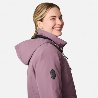 A woman with blonde braided hair wears the Free Country Women's Back of Bell 3-in-1 Systems Jacket in mauve, smiling as she looks over her shoulder against a plain light background.