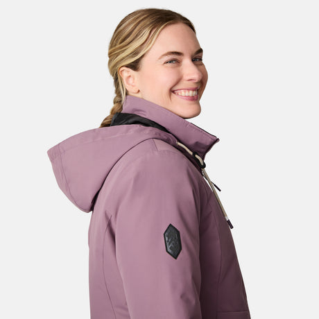 A woman with blonde braided hair wears the Free Country Women's Back of Bell 3-in-1 Systems Jacket in mauve, smiling as she looks over her shoulder against a plain light background.