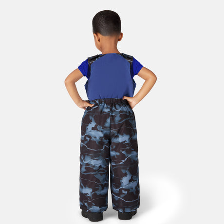 A young child with short hair, hands on hips, wears the Free Country Toddler Boys' Out of Bound Jacket and Bib Pant Ski Set in blue with black boots, facing away against a plain light background.