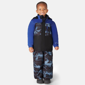 A young child smiles while wearing the Free Country Toddler Boys' Out of Bound Jacket and Bib Pant Ski Set with black boots, standing against a plain white background.