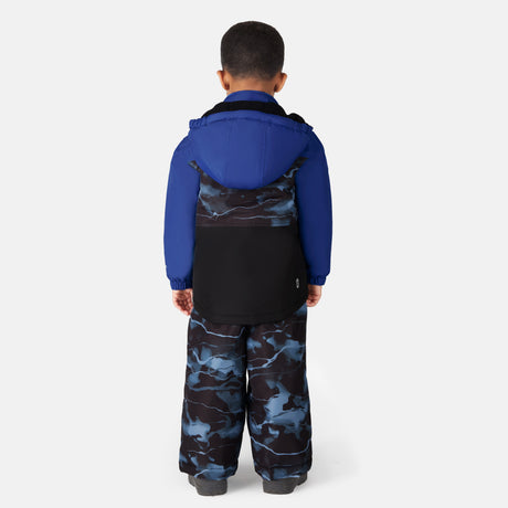 A toddler faces away, wearing the Free Country Toddler Boys' Out of Bound Jacket and Bib Pant Ski Set in blue camo, displayed against a plain white background.