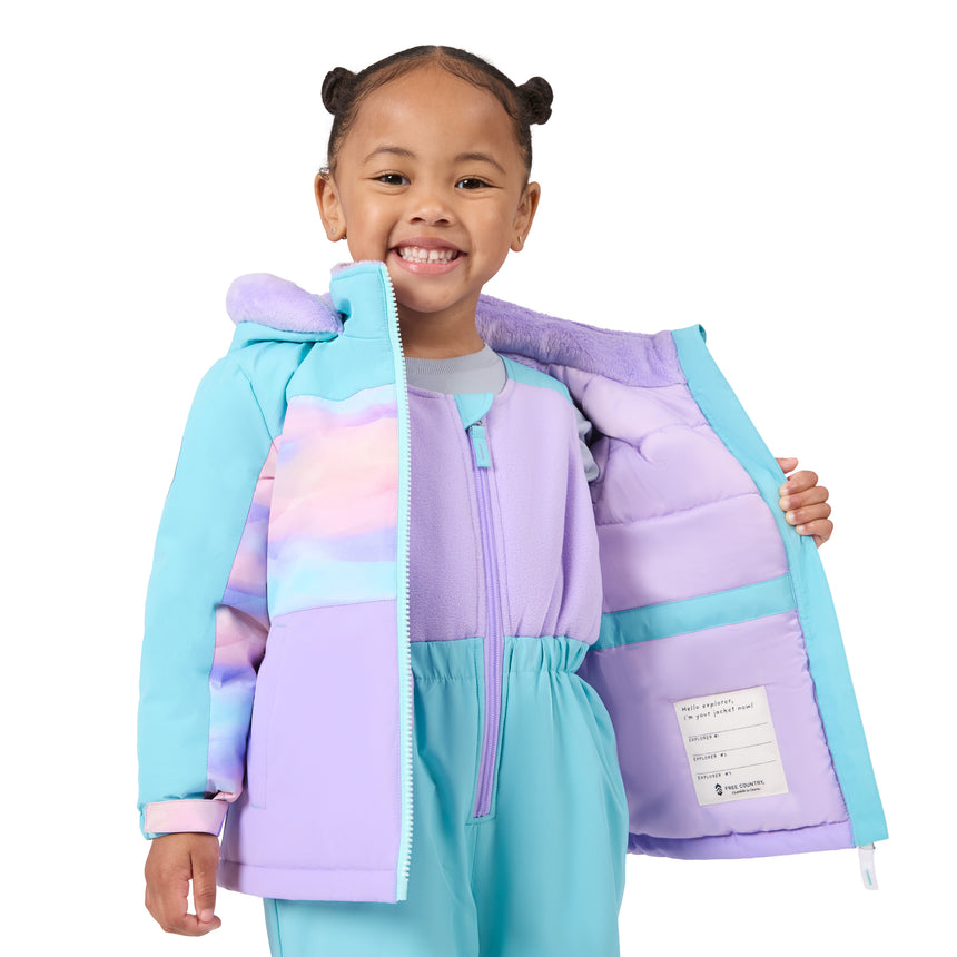 A young girl with her hair in two buns smiles while holding open a light blue and lavender puffer jacket to show the interior lining. The jacket features pastel color-blocked panels in purple, pink, and light blue, with a matching lavender hood and a white interior label.