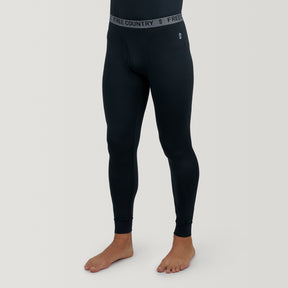 A man wears Free Country Men's Microtech® Heat Cocarber® Coffee Base Layer Bottoms, featuring black thermal leggings with a gray elastic waistband reading 'FREE COUNTRY,' made from moisture-wicking fabric for comfort.