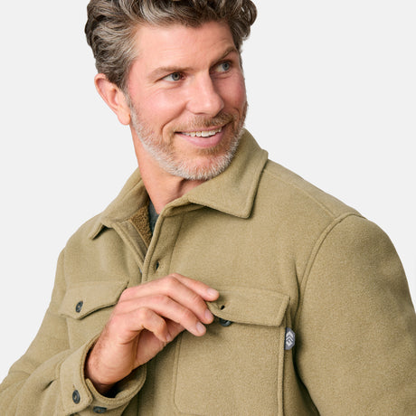 [Kolby is 6'2" wearing size M.] Men’s Free Country tan button-up jacket, sherpa-lined for added warmth, featuring dual flap chest pockets and thick, textured outer fabric—layered over a dark shirt and paired with blue jeans for a rugged, cold-weather look with timeless outdoors appeal.