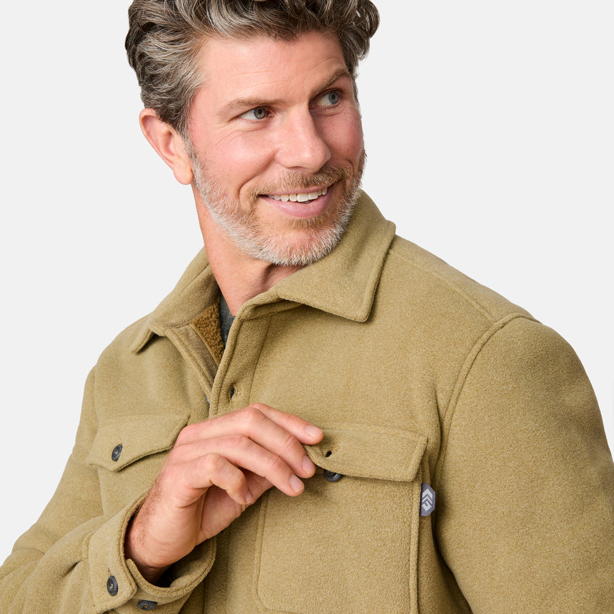 [Kolby is 6'2" wearing size M.] Men’s Free Country tan button-up jacket, sherpa-lined for added warmth, featuring dual flap chest pockets and thick, textured outer fabric—layered over a dark shirt and paired with blue jeans for a rugged, cold-weather look with timeless outdoors appeal.