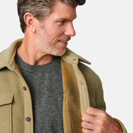 [Kolby is 6'2" wearing size M.] Men’s Free Country tan button-up jacket, sherpa-lined for added warmth, featuring dual flap chest pockets and thick, textured outer fabric—layered over a dark shirt and paired with blue jeans for a rugged, cold-weather look with timeless outdoors appeal.
