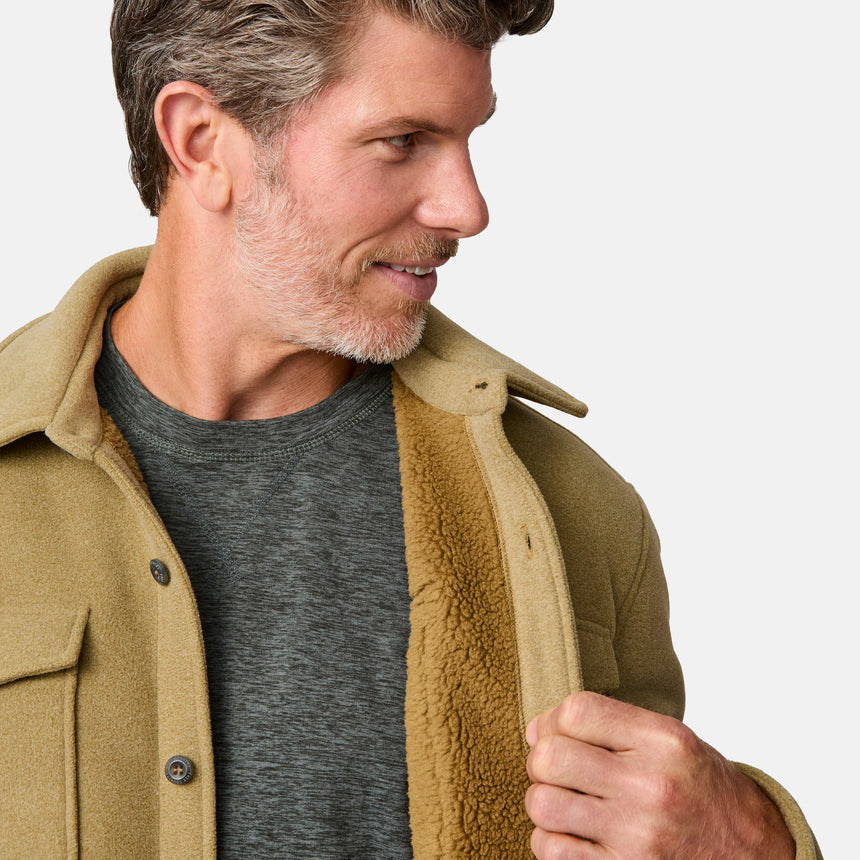 [Kolby is 6'2" wearing size M.] Men’s Free Country tan button-up jacket, sherpa-lined for added warmth, featuring dual flap chest pockets and thick, textured outer fabric—layered over a dark shirt and paired with blue jeans for a rugged, cold-weather look with timeless outdoors appeal.