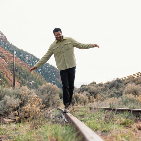 Man balancing on a train rail with a mountainous landscape in the background