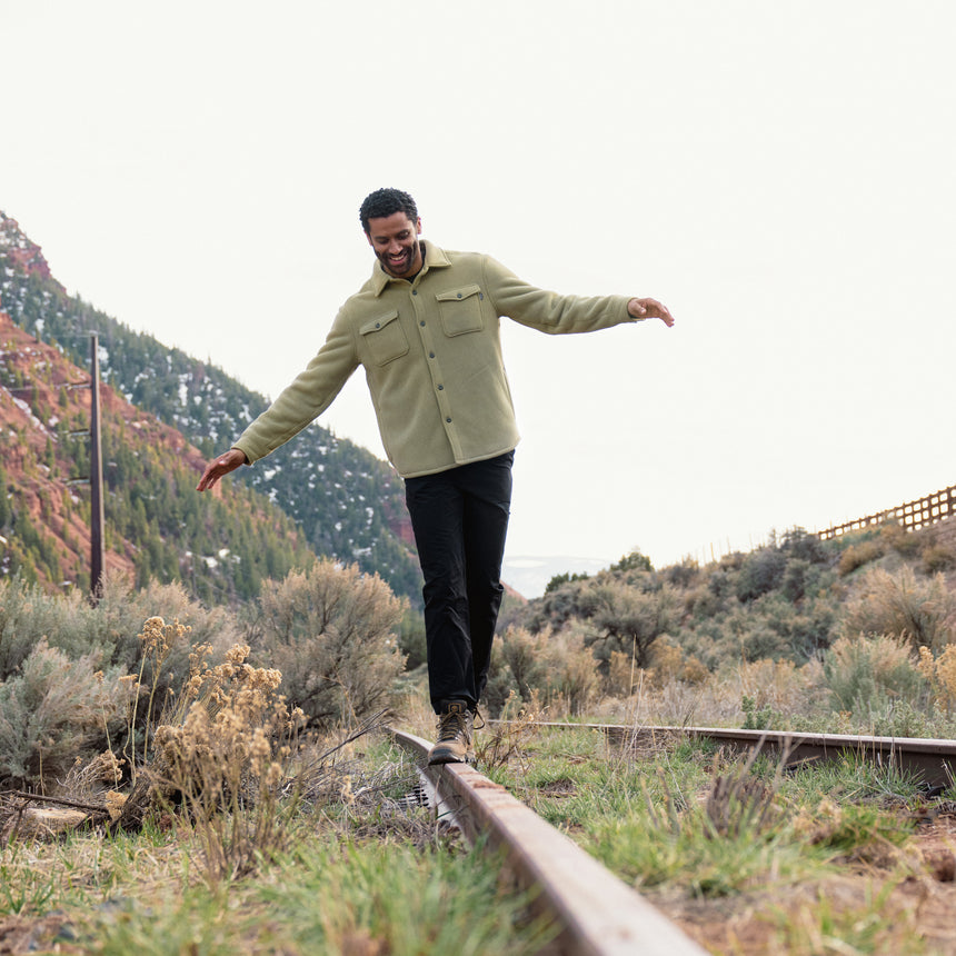 Man balancing on a train rail with a mountainous landscape in the background