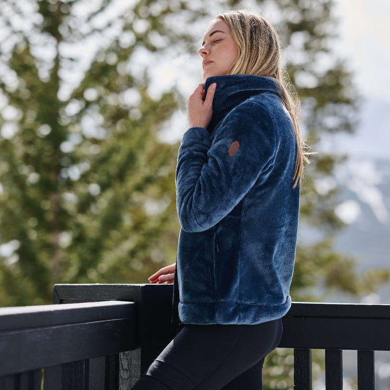 Woman wearing a blue Frosted Butter Pile® fleece jacket on a blurred nature background