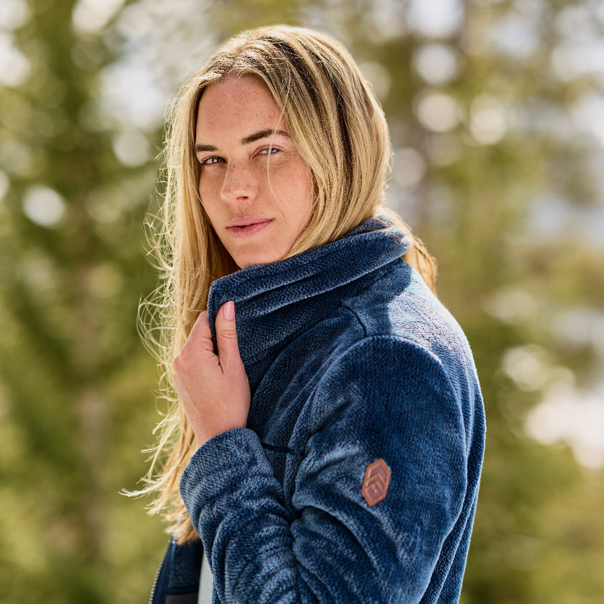 Woman wearing a blue Frosted Butter Pile® fleece jacket on a blurred nature background