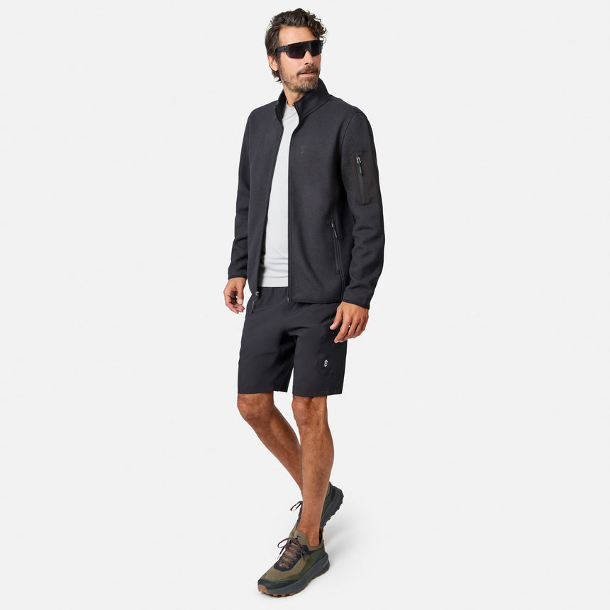 [Model is wearing size M.] A man modeling a dark gray outdoor zip-up jacket, matching dark gray shorts, a white t-shirt, and hiking shoes against a light gray background.