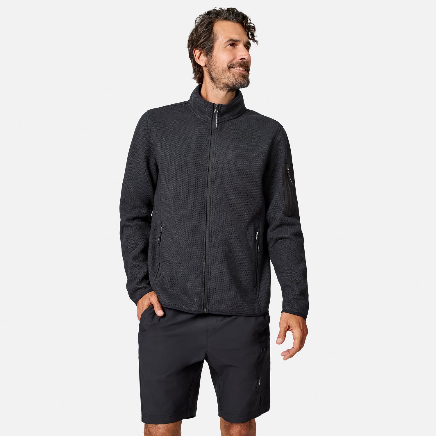 [Model is wearing size M.] A man wearing a dark charcoal zip-up fleece jacket and matching dark shorts, standing against a light gray studio background.
