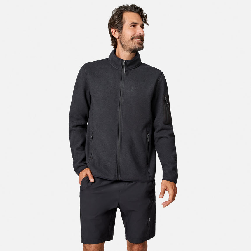[Model is wearing size M.] A man wearing a dark charcoal zip-up fleece jacket and matching dark shorts, standing against a light gray studio background.