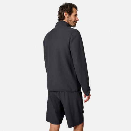[Model is wearing size M.] A man wearing a dark charcoal gray long-sleeve quarter-zip fleece and matching dark shorts, shown from a three-quarters back view against a light gray studio background.