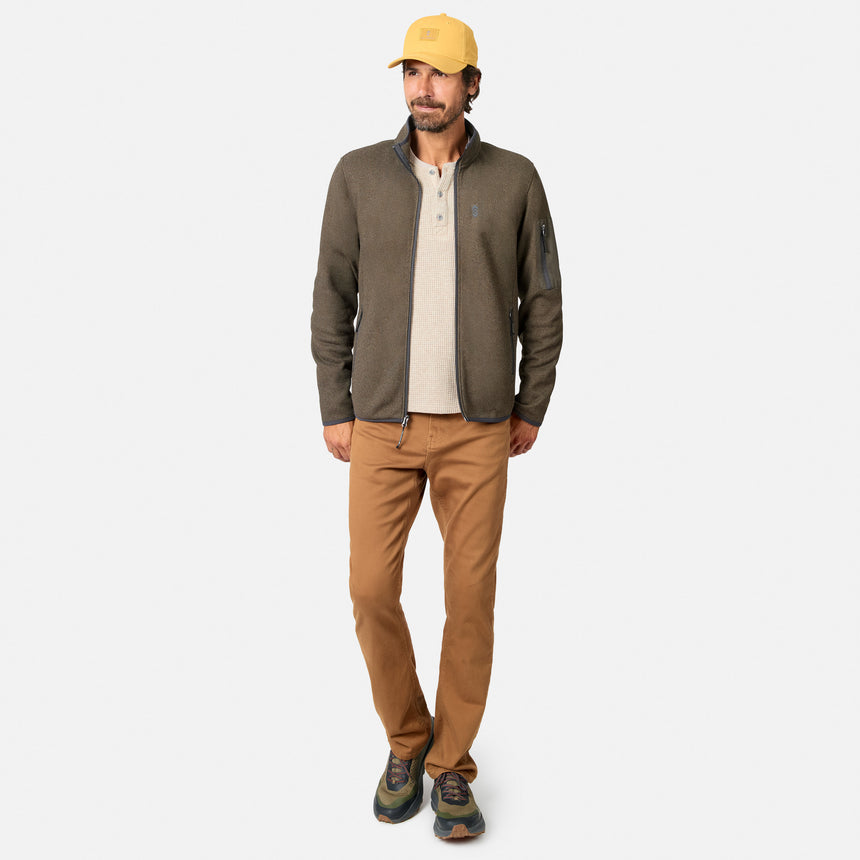 [Model is wearing size M.] A man modeling a dark olive green quarter-zip fleece jacket over a beige henley shirt, paired with brown pants, hiking shoes, and a yellow baseball cap, against a light gray background.