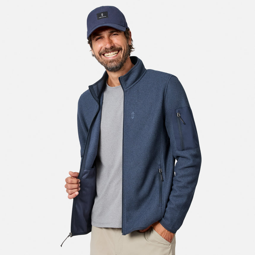 [Model is wearing size M.] A smiling man wearing a navy blue zip-up fleece jacket over a gray t-shirt, khaki pants, and a matching navy baseball cap, photographed against a clean light gray studio background.