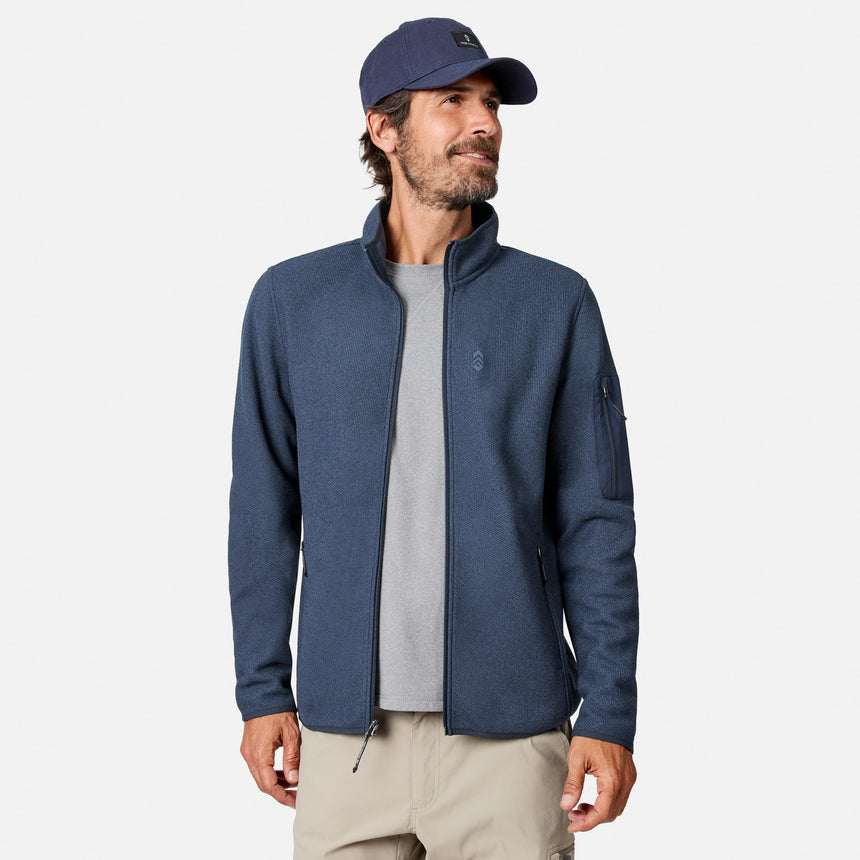 [Model is wearing size M.] A man wearing a heathered navy blue zip-up fleece jacket over a gray t-shirt, khaki pants, and a navy baseball cap, photographed against a clean light gray studio background.