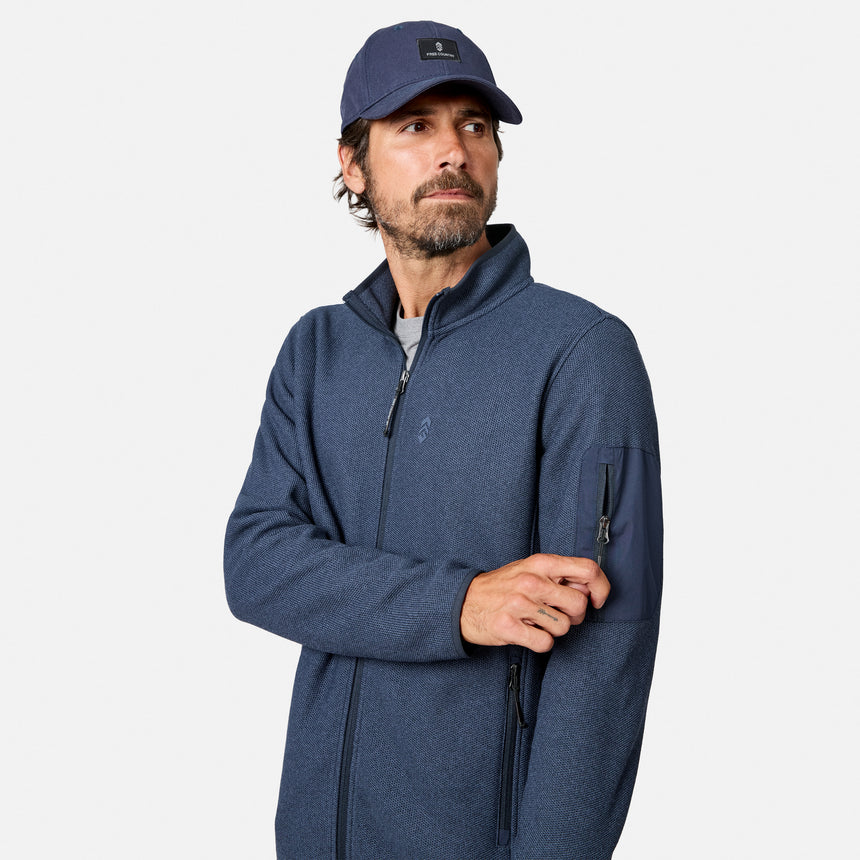 [Model is wearing size M.] A man wearing a heathered navy blue quarter-zip fleece jacket and a matching navy blue baseball cap, photographed against a clean light gray studio background.
