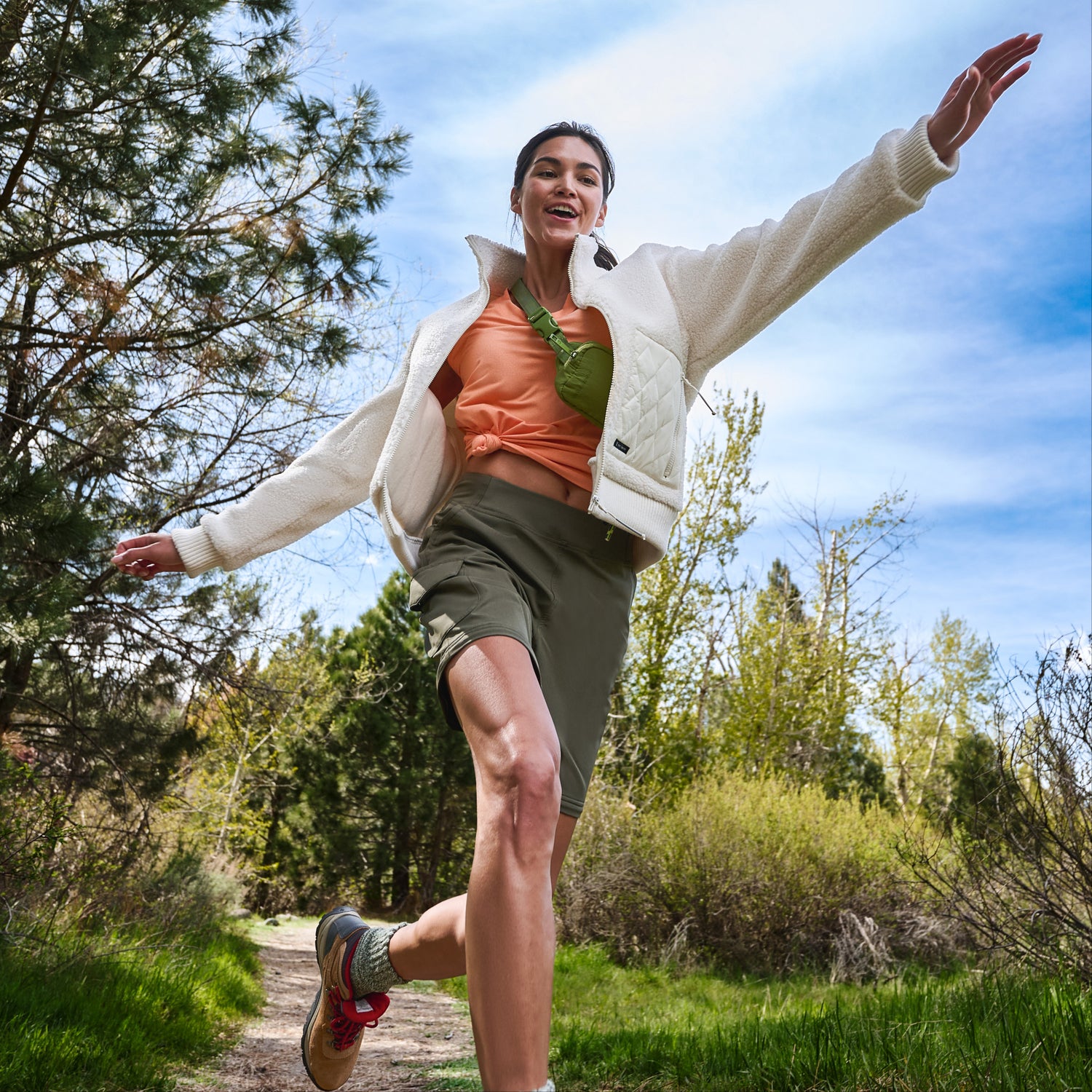 Woman leaping playfully on a forest path in a white fleece jacket