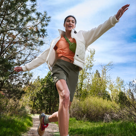 Woman leaping playfully on a forest path in a white fleece jacket