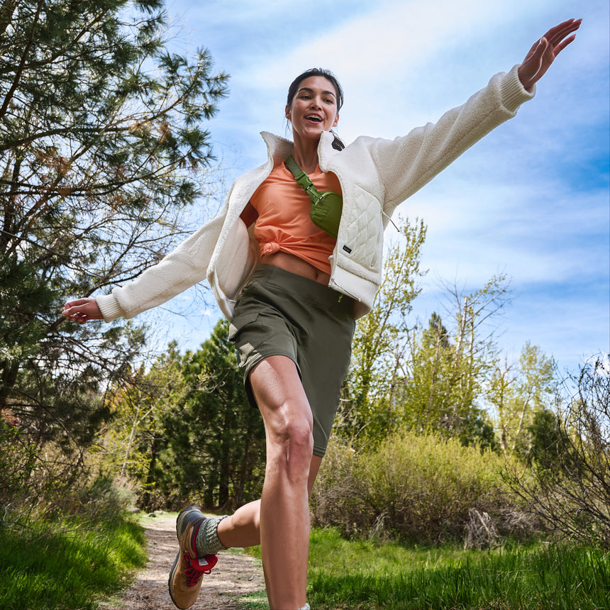 Woman leaping playfully on a forest path in a white fleece jacket