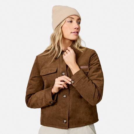 A woman wearing a brown suede jacket and a beige beanie, posing against a light gray studio background.
