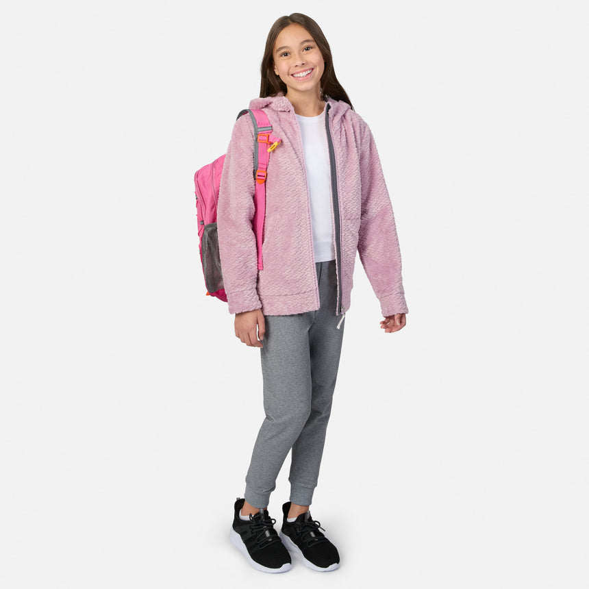 A girl wearing a pink Girls’ Braided Butter Pile® Jacket, a white t-shirt, gray joggers, and black sneakers, with a pink backpack on her back.