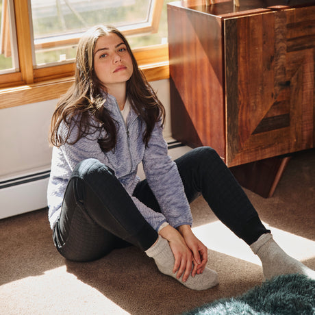 Woman sitting on the floor in a room with wooden furniture and large windows.