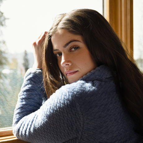 Woman wearing a blue quilted fleece jacket by a window with natural light